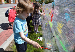 Dzieci w ogrodzie malują na folii, na pierwszym planie malujący chłopiec
